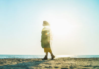 Rear view of man standing on beach against clear sky