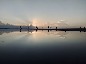 Silhouette people on lake against sky during sunset