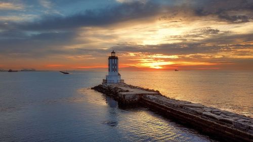 Lighthouse at sea against sky during sunset
