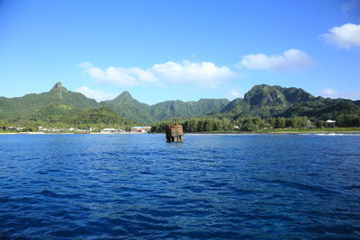 Scenic view of sea by mountains against blue sky