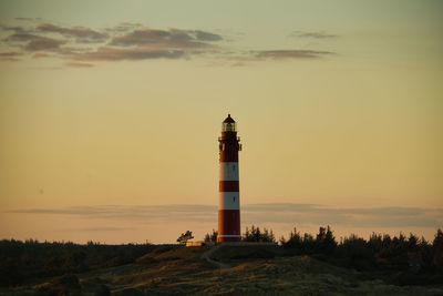 Lighthouse by building against sky during sunset