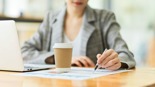 Midsection of woman using mobile phone while sitting on table