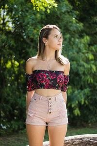 Thoughtful teenage girl looking away while standing against trees in park