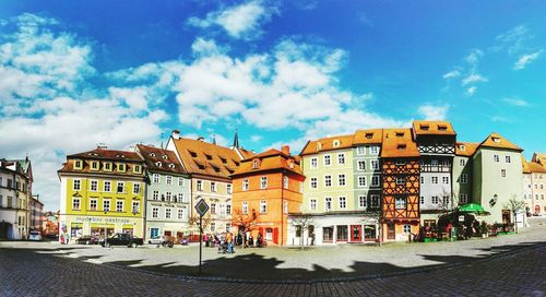 Buildings by street against blue sky in city on sunny day