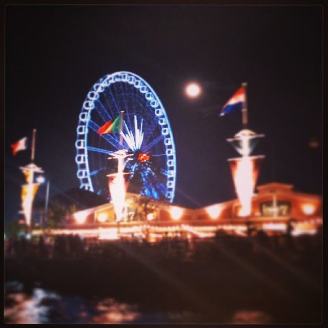 illuminated, night, arts culture and entertainment, amusement park, amusement park ride, ferris wheel, transportation, city, mode of transport, land vehicle, sky, built structure, blurred motion, building exterior, outdoors, clear sky, glowing, architecture, motion, travel