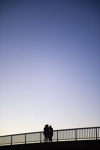 Silhouette woman walking on bridge against clear blue sky