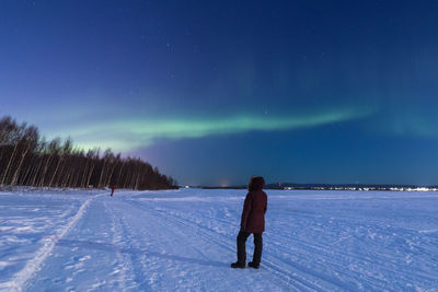 Rear view of woman walking on snow field against sky at night