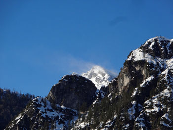 Low angle view of snowcapped mountains against clear blue sky