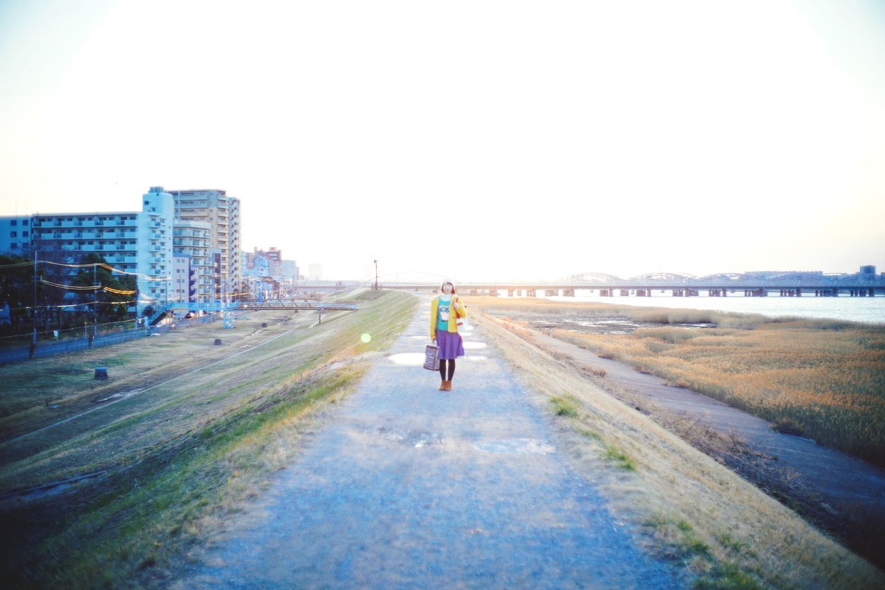 full length, clear sky, walking, copy space, rear view, building exterior, lifestyles, the way forward, architecture, built structure, road, street, leisure activity, men, city, day, casual clothing, diminishing perspective