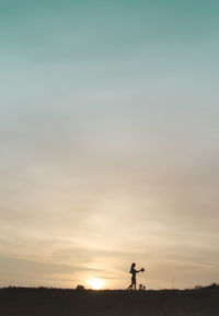 Silhouette man standing by tree against sky during sunset