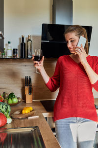 A young girl stands in the kitchen and is distracted from cooking by talking on a mobile phone 