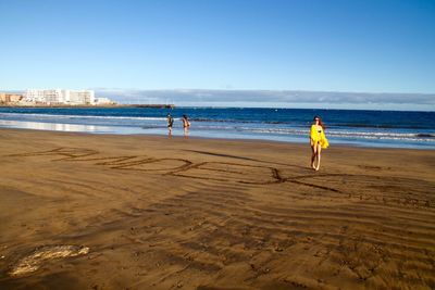 Woman walking at beach against clear sky on sunny day