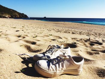 Close-up of shoes on beach against clear sky