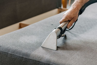 Close-up image of professional cleaning service doing a deep clean of sofa in living room.