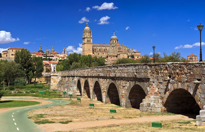 Arch bridge by buildings against blue sky