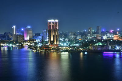 Illuminated buildings by river against sky at night