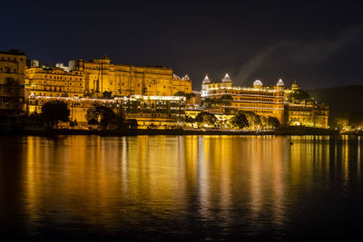 Illuminated buildings by river against sky at night
