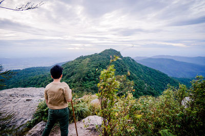 Rear view of man holding stick while standing in rock against sky