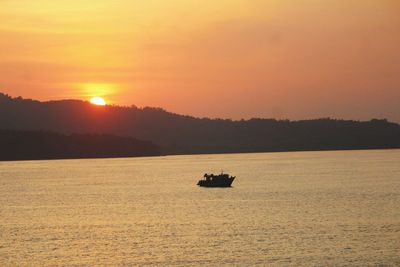 Silhouette boat in sea against orange sky