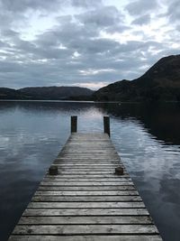 Pier over calm lake against cloudy sky