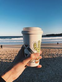 Person holding drink at beach against sky