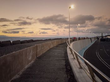 Empty road by street against sky during sunset