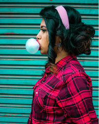 Side view of woman blowing bubble against wall