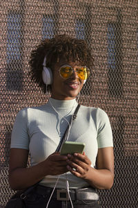 Cool young latin american woman with afro hair and glasses smiling listening to music on smartphone 