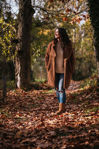 Beautiful brunette woman walking on a path full of dry leaves on autumn.