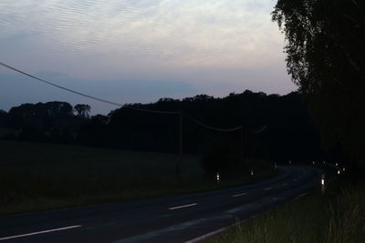 Road by silhouette trees against sky at sunset