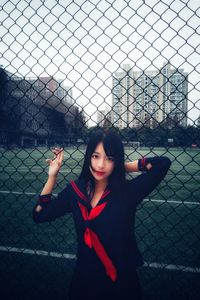 Portrait of woman standing by chainlink fence