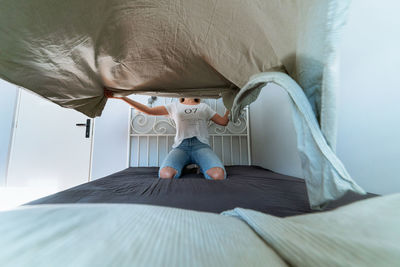 Rear view of woman sitting on bed at home