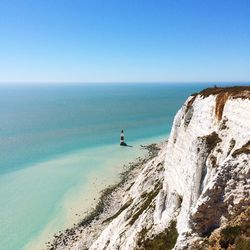 High angle view of lighthouse amidst sea and mountain against blue sky