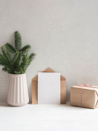 Christmas tree branches vase, open  envelope and empty postcard near the gray wall and wrapped gift. 