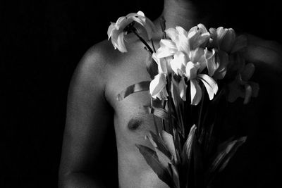 Midsection of shirtless man holding flowers while standing in darkroom