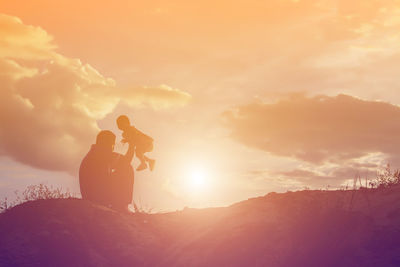 Silhouette man photographing on mountain against sky during sunset