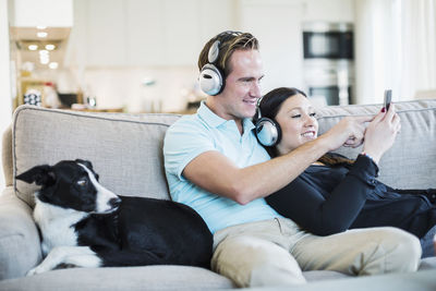 Couple listening to headphones with dog sitting on sofa