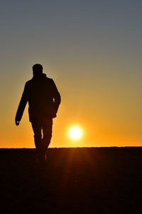Silhouette man waling on field against sky during sunset