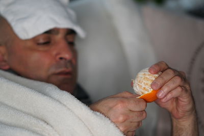 Close-up of man having orange while lying on sofa