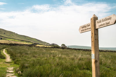 Road sign on field against sky