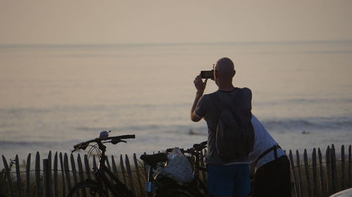 Rear view of man photographing sea with smart phone against sky