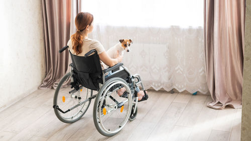 Rear view of woman sitting on wheelchair with dog