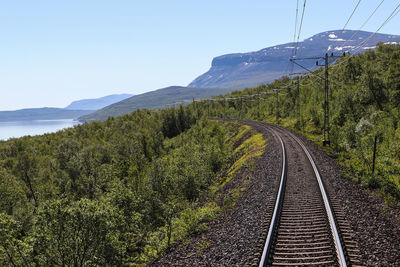 Railroad tracks by mountain against clear sky