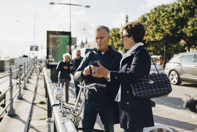 Senior couple using mobile phone while standing on sidewalk in city