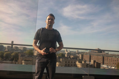 Reflection of man photographing with camera on window in city