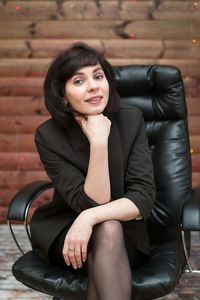 An adult brunette woman in a black formal jacket is sitting in an office chair  wooden background.