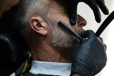 Cropped hands of barber cutting beard of man at salon