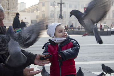 Smiling son looking at pigeons by father in city during winter