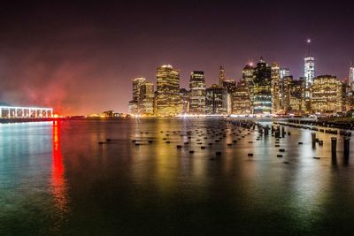 Illuminated buildings by sea against sky at night