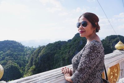 Portrait of smiling young woman standing on mountain against sky